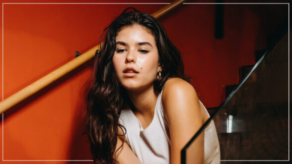 A brunette girl looking down while sitting on stairs in front of an orange red background