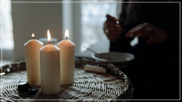 Moody image of a person standing behind 3 lit candles