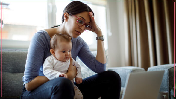 Image of a stressed out mother with her hand to her forehead and holding her kid and looking at a laptop