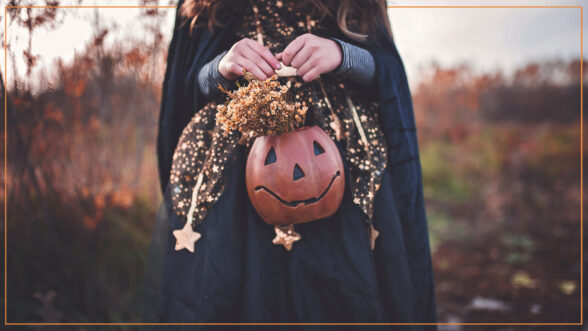 Image of a girl wearing a witch costume and holding a pumpkin shaped basket with flowers in it