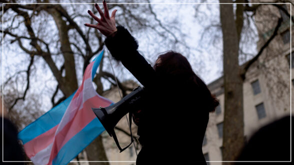 Image of a woman holding up a Trans Pride flag and talking through a megaphone